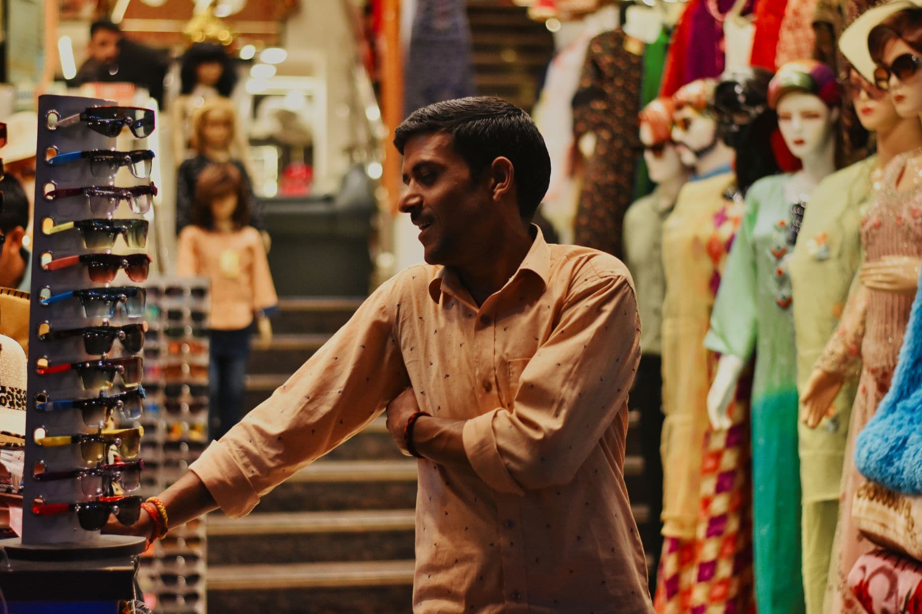A shopper reaching for a rack of sunglasses in a densely stocked variety shop