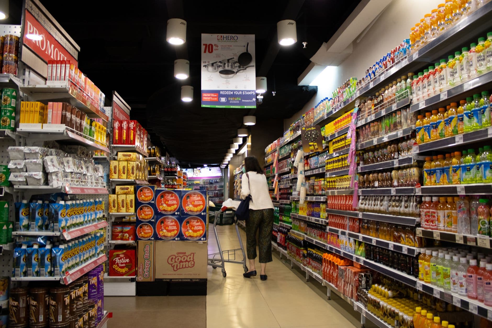 A shopper walking a densely stocked discount-store aisle beneath a sale sign