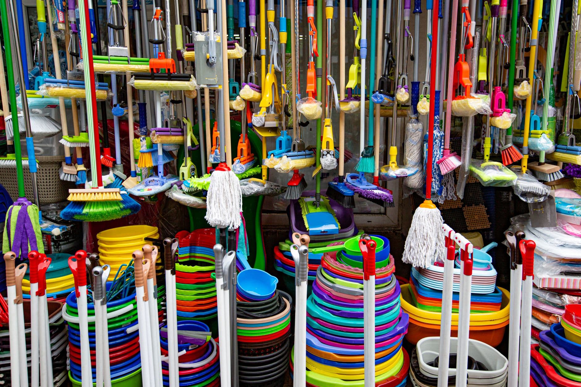 A dense colorful display of mops, brushes, buckets and household baskets
