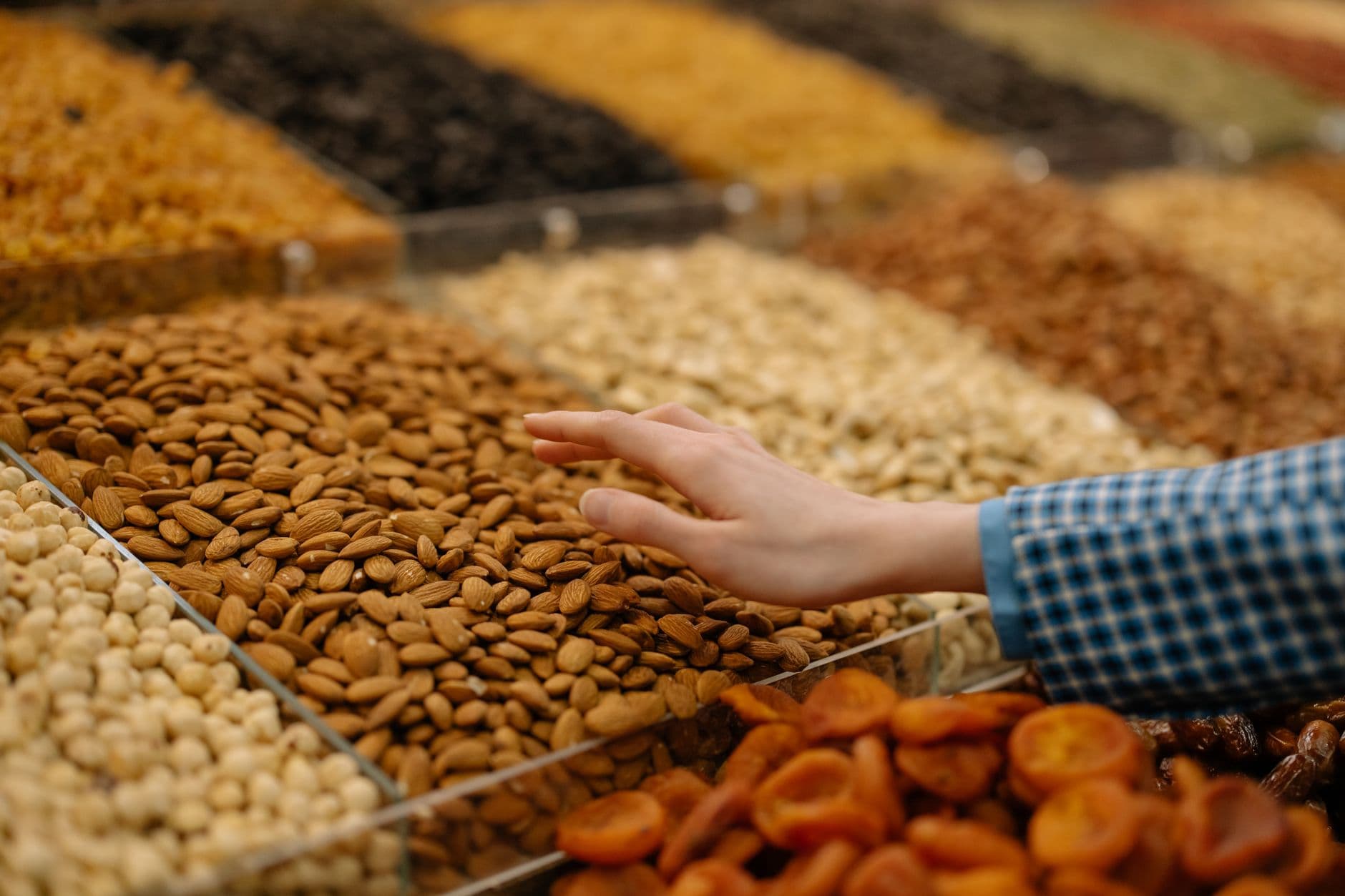 A hand reaching into open bins of nuts and dried goods
